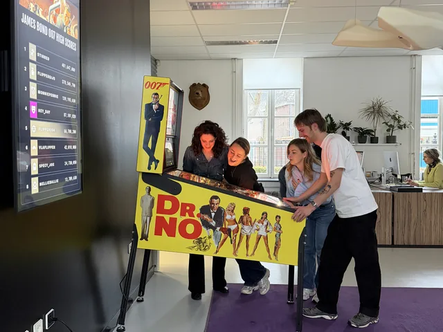 Flipperkast huren voor op kantoor: het team van Heyalo in Tilburg aan de James Bond 007 met het leaderboard op het scherm